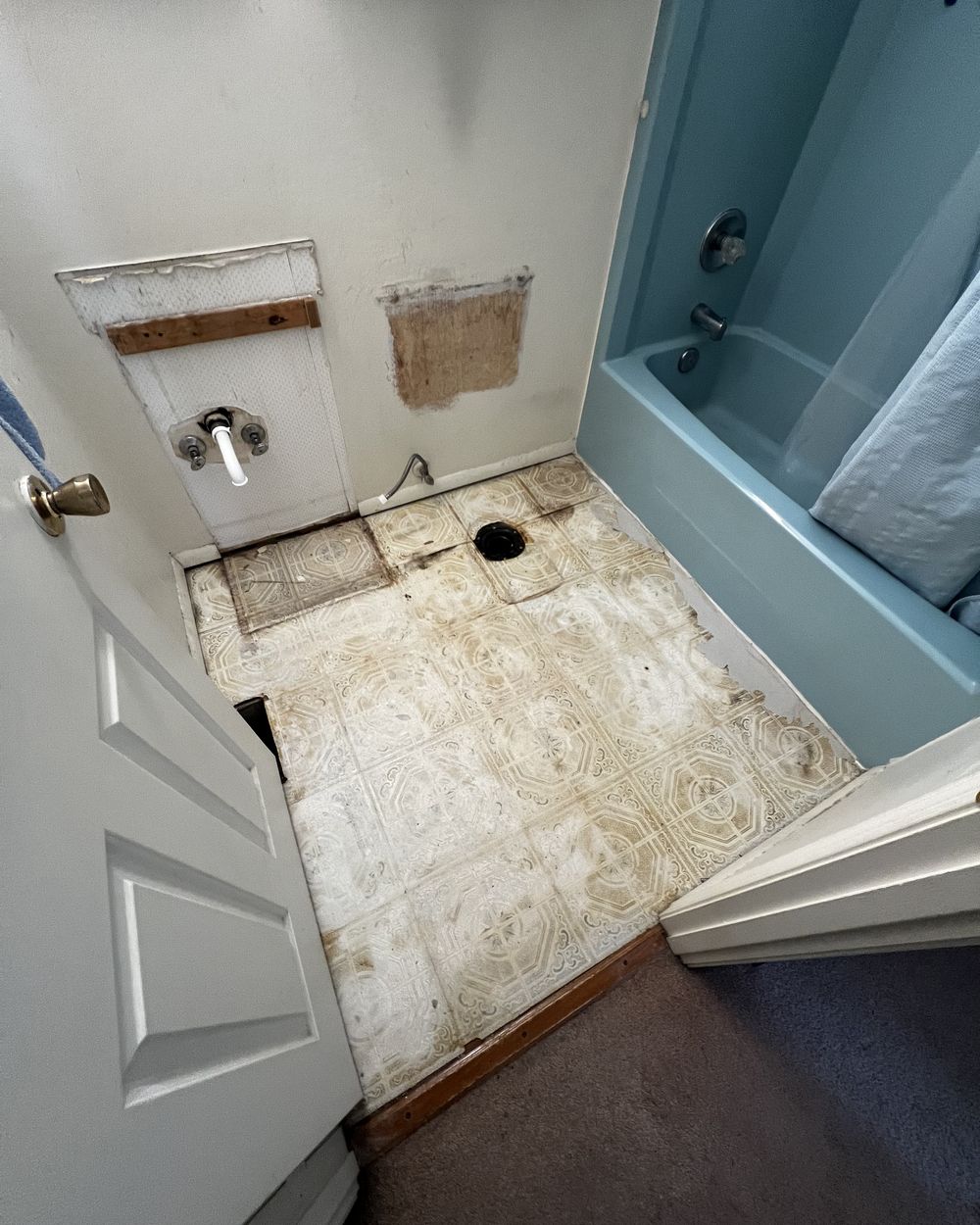 A bathroom stripped to the subfloor with the vanity and toilet pulled out.