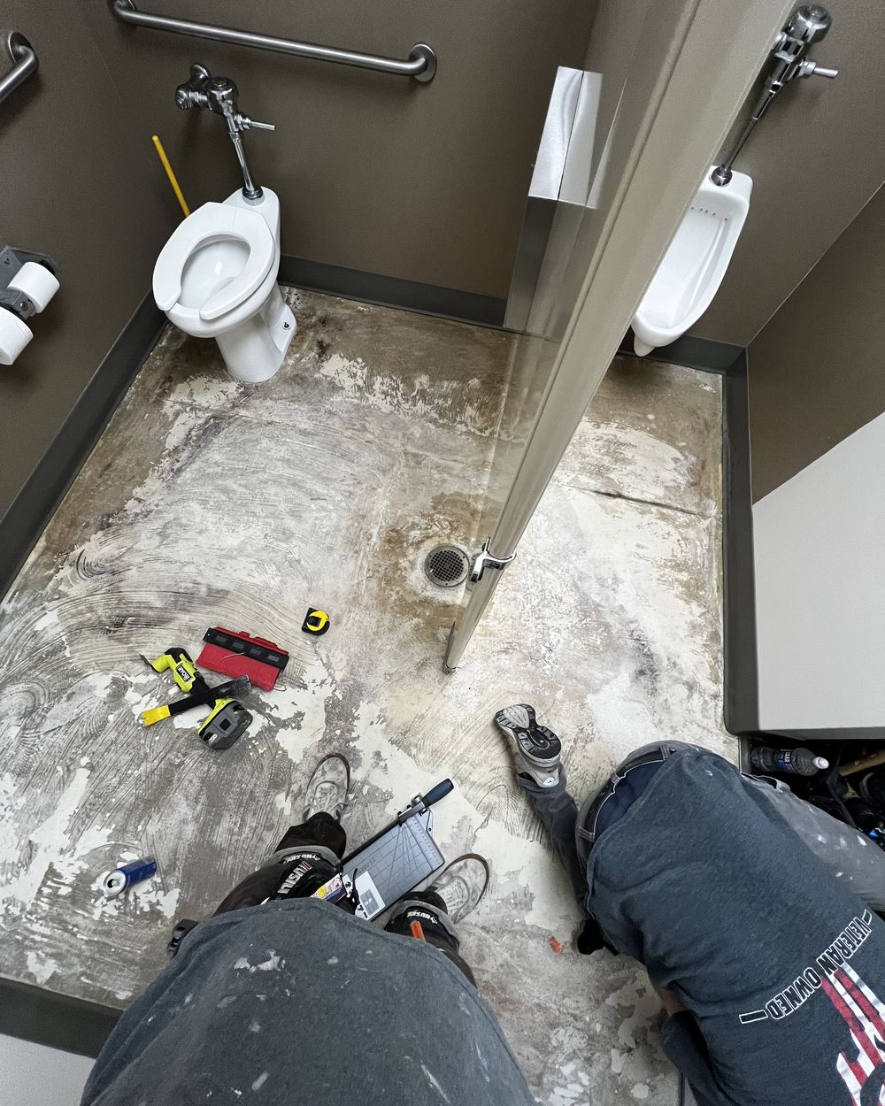 A commercial restroom floor stripped back to bare slab with old adhesive showing.
